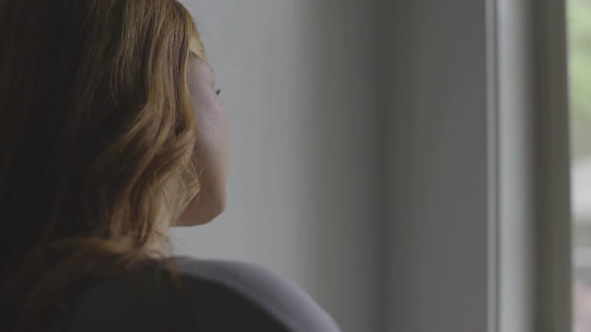 The young female with dishwater blonde hair is sitting with her head tilted looking out the window contemplating on what appears to be a sunny day