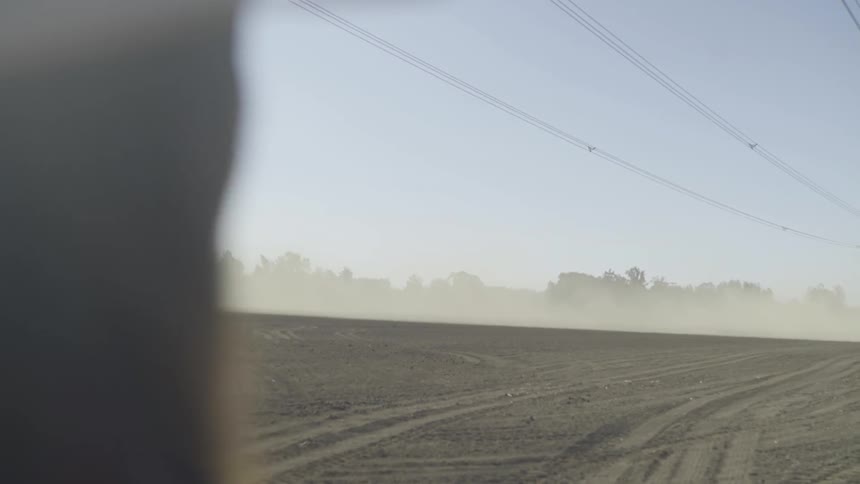 The man is standing in a dirt field watching the dust storm under the power lines