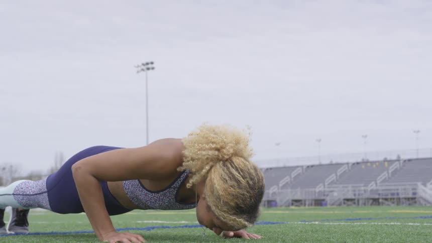 Young woman in athletic wear does push ups on outdoor athletic field