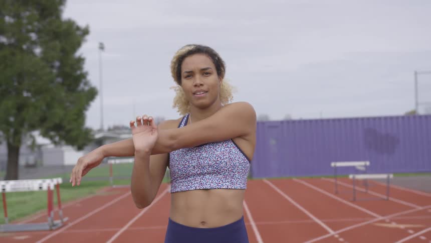 Woman stretches her arms while standing on a track