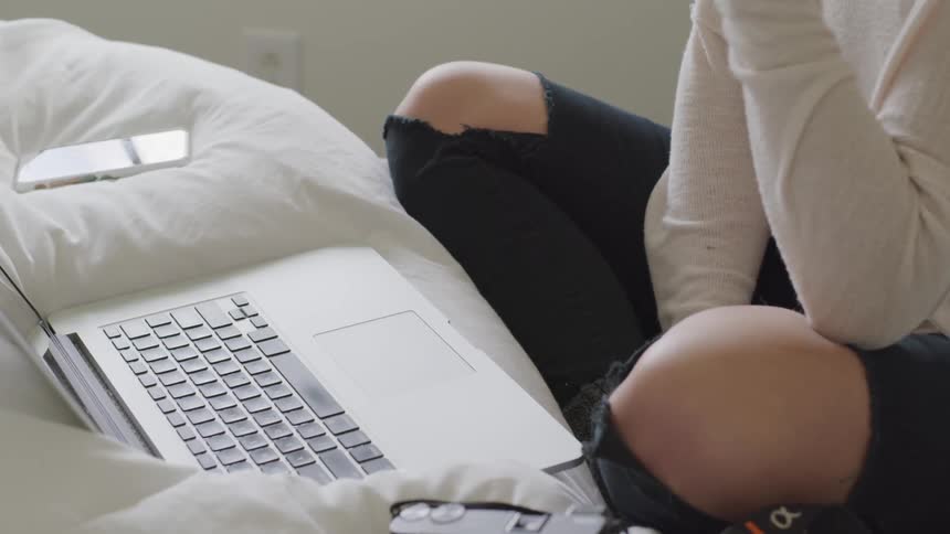 A woman sitting on a bed using a laptop