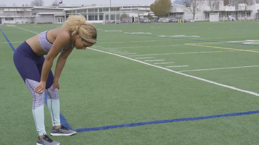 A woman touches her knees and breathes on the field