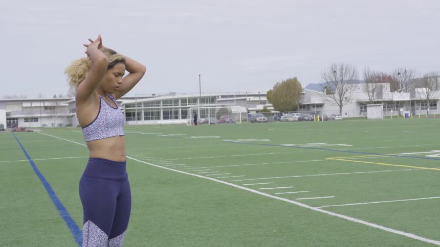 A female on a football field stretching her arms