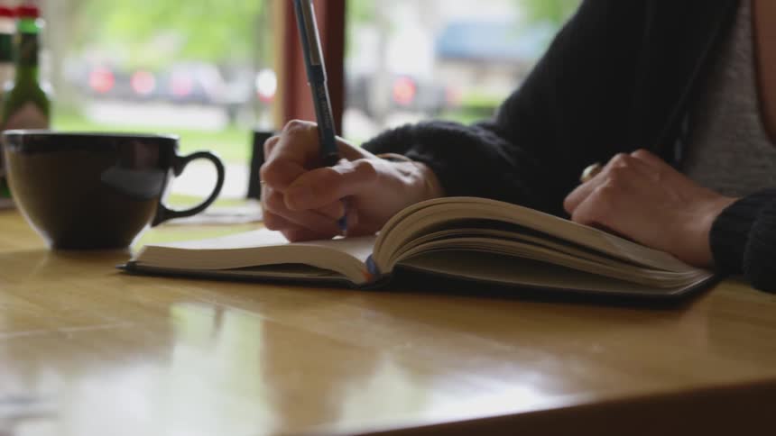 A female sitting at a diner table writing in a journal