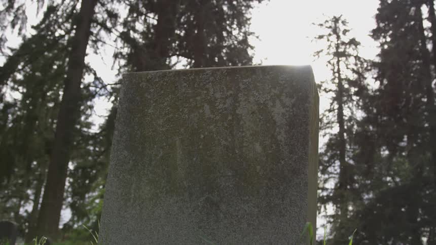 Sunlight shines over an old stone headstone in a cemetery