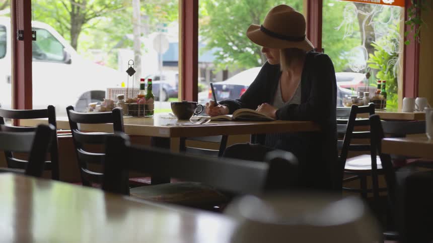 A woman sitting in a diner writing in a book