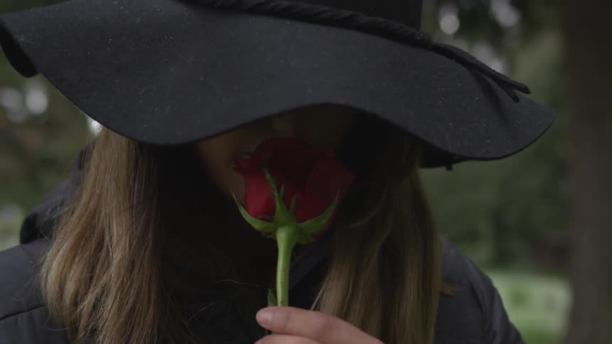 A woman brings a rose up to her nose and smells it