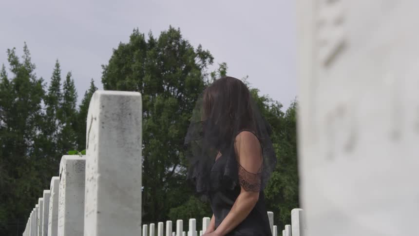 A woman in black is standing at the grave in the cemetery