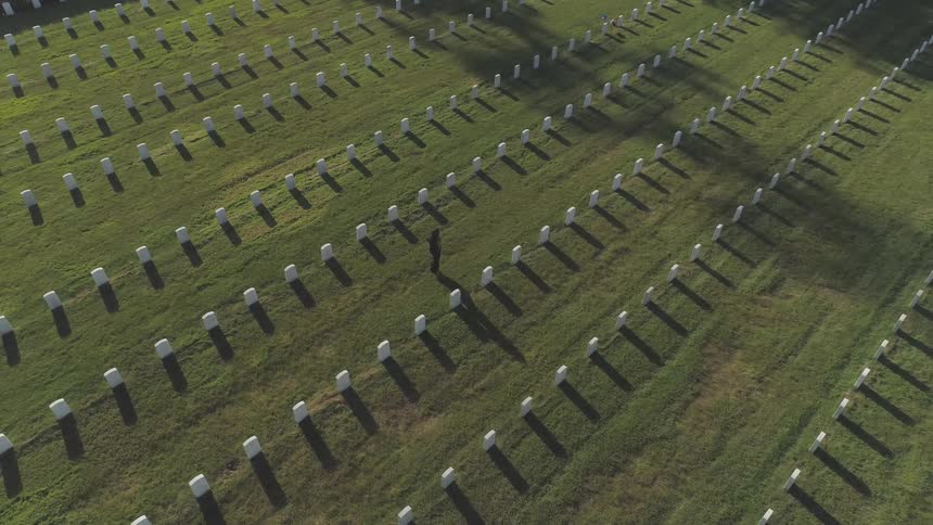 A woman walks between rows of white headstones on green grass