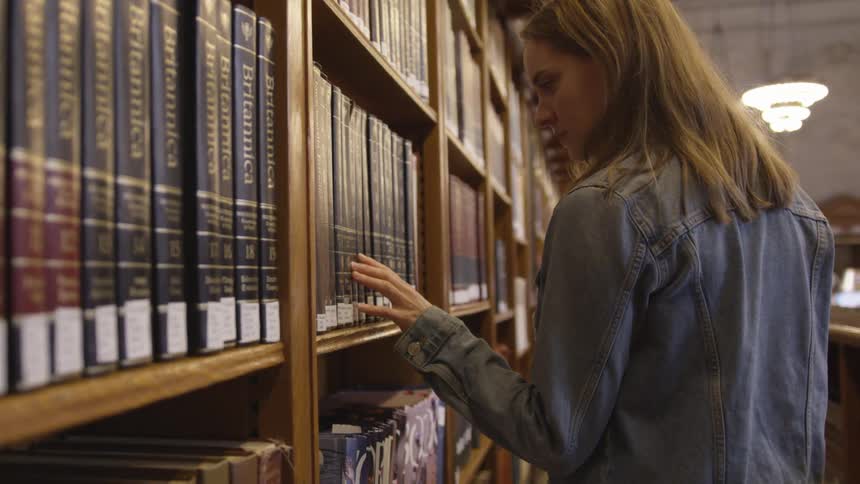 Woman looking and touching the books of a book library