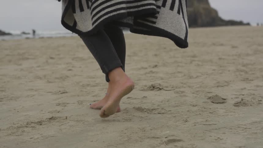 The woman is walking barefoot in the sand at the beach
