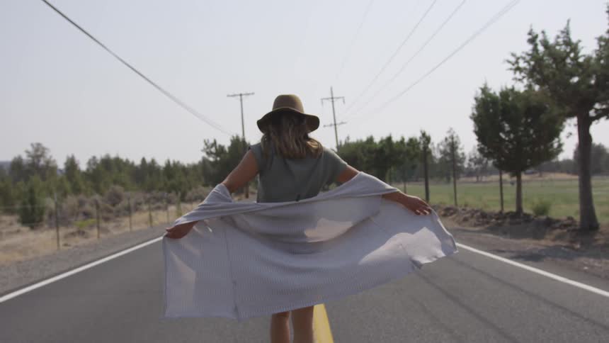 A woman walking down the center of a road lined with trees