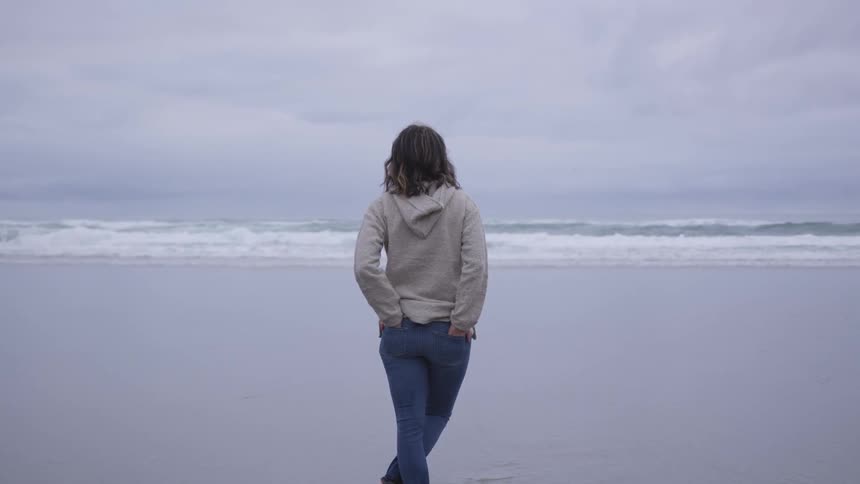 A woman is standing on a beach and looking out onto the ocean