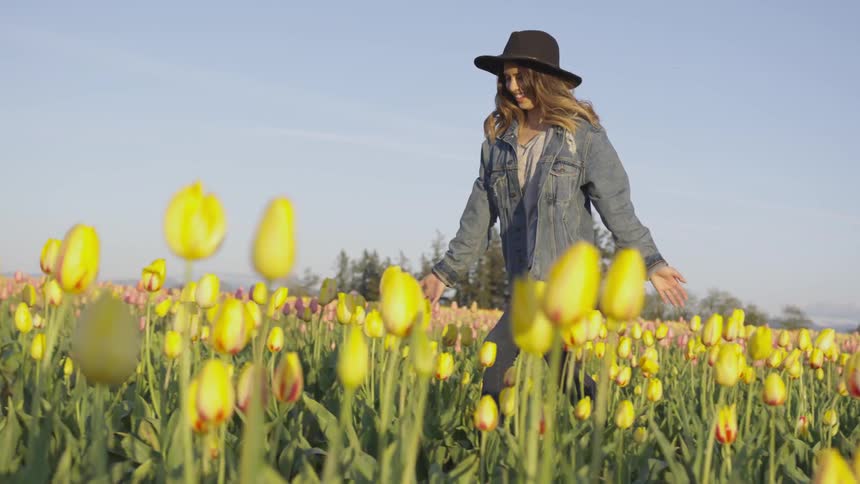 A woman laughs and runs through a field of flowers