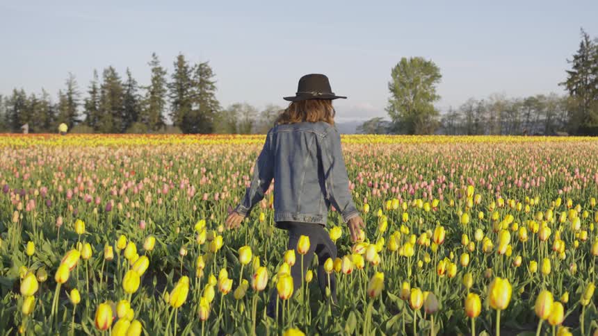 A woman in a denim jacket and black hat runs in a field of tulips