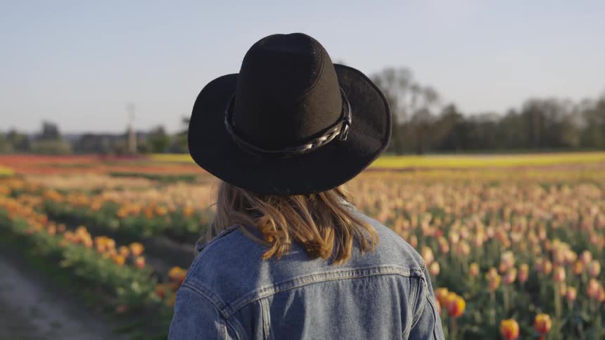 A woman walks down a road next to a field of flowers