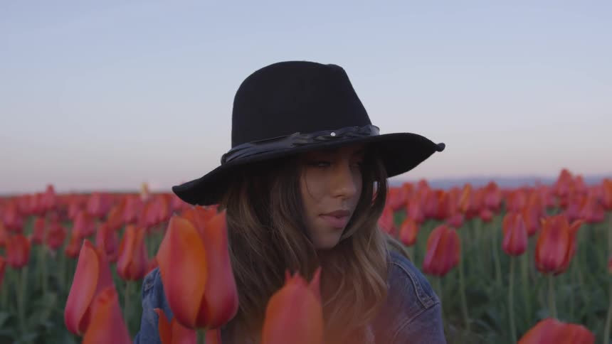 A woman in a black hat sits in a field of red tulips
