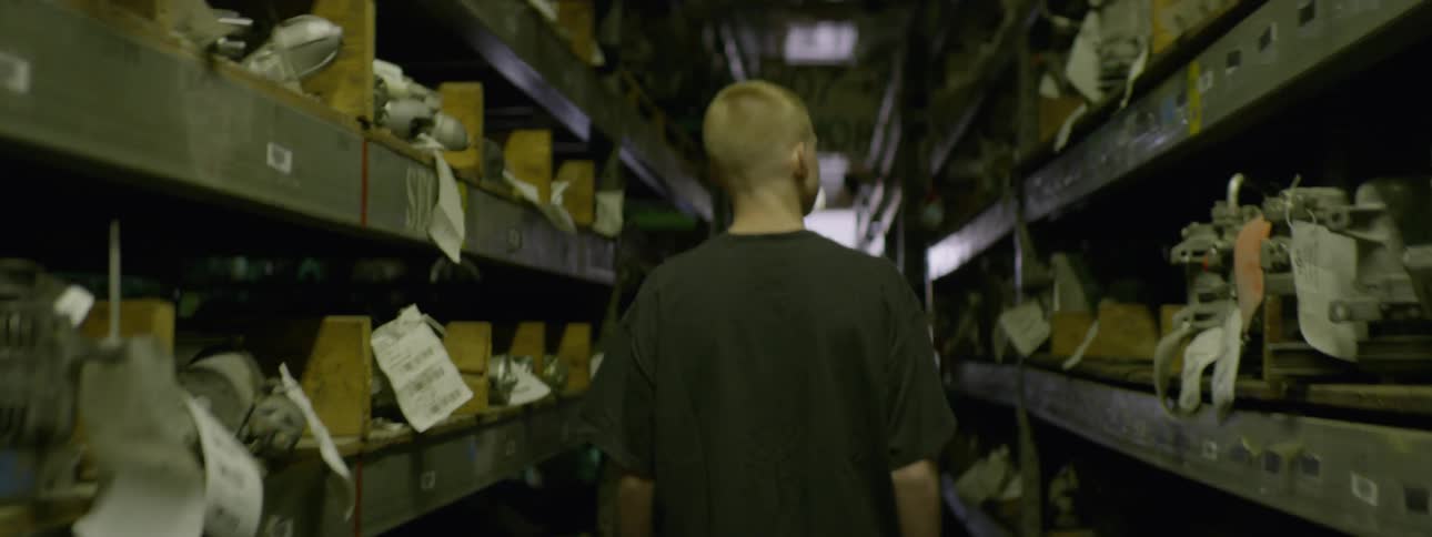 A young man walks between the tall shelving units in a warehouse