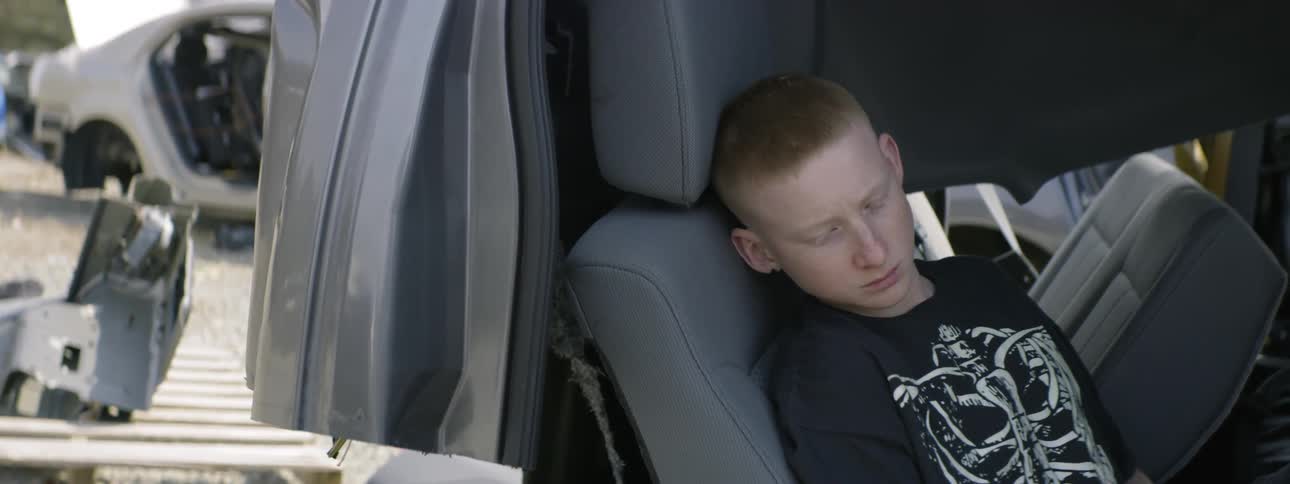A boy sitting in a car in a junkyard