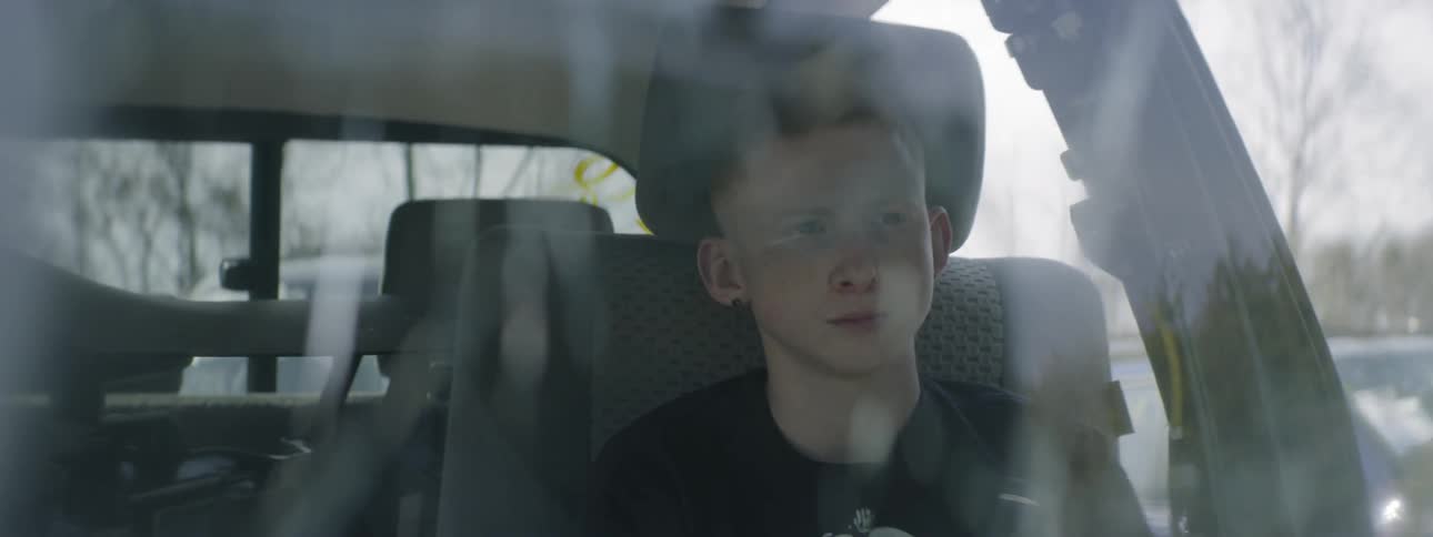 A white teenager sits inside of a truck with a broken windshield