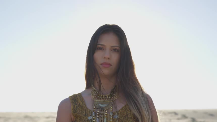 Woman wearing a decorative necklace stands in a field under a blue sky