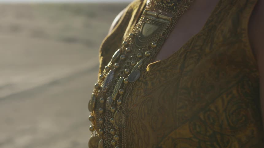 A woman's chest is present with gold jewels