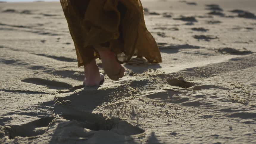 A person walks across sand barefooted