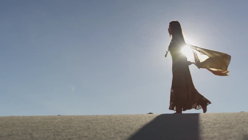 Woman walks in the sand and her cape flutters in the wind behind her