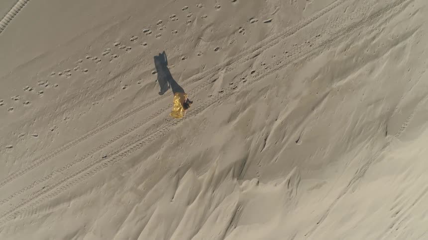 Woman walks across sand dotted with footprints