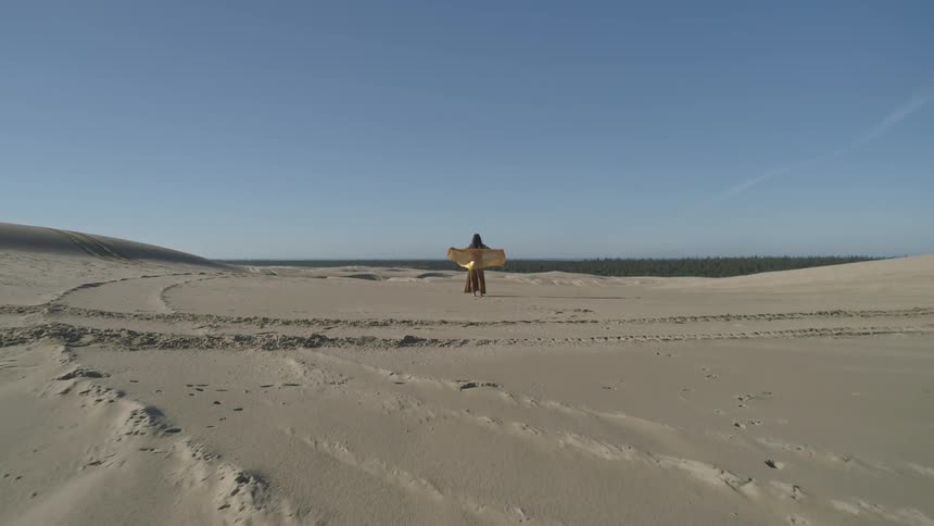 A woman stands on a large sandy area with a scarf