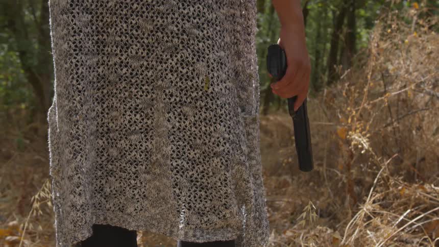 Woman holding a handgun in a field of dead tall grass