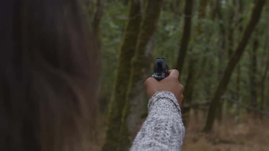 Woman points a gun at empty space in a forest