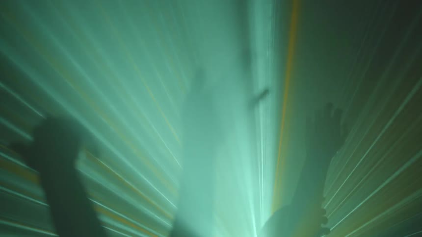 Peoples raised hands dance in colored laser lights
