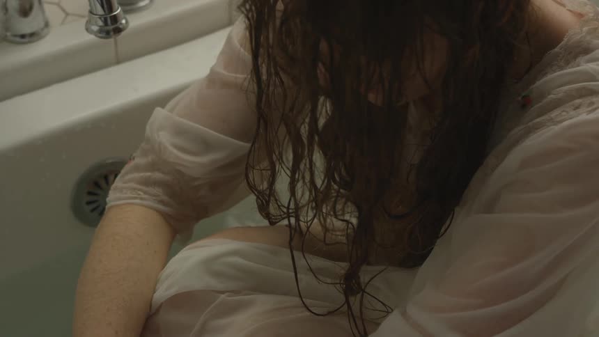 A soaking wet white woman huddles in a bathtub