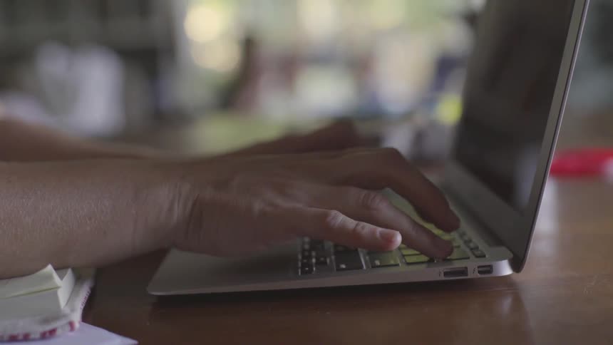 The hand is typing keys on the laptop that is sitting on the table and in a cafe