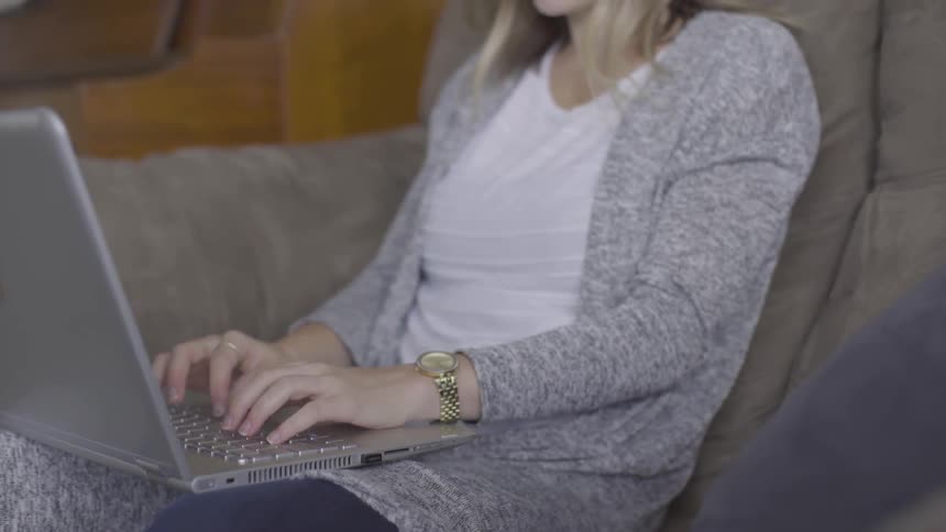 Woman sits on couch typing on laptop