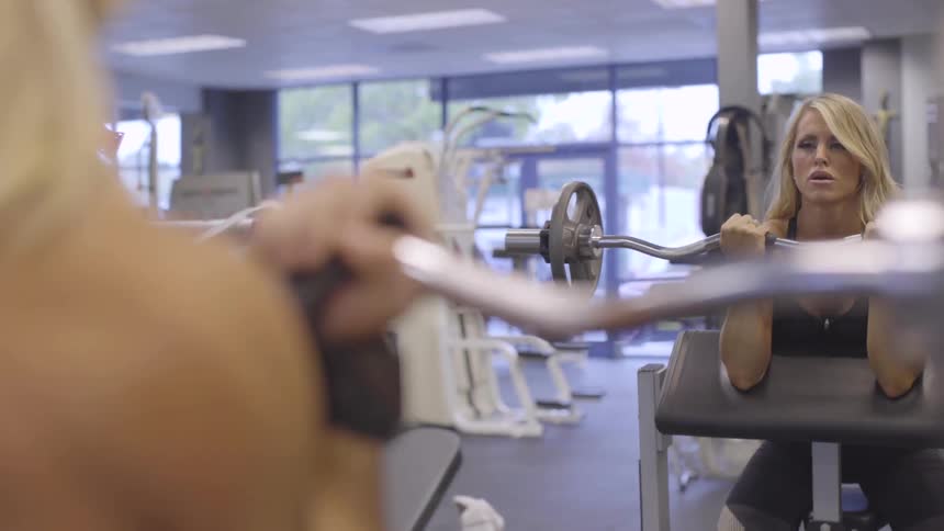 Blonde female doing bicep curls workout with a bar at the gym