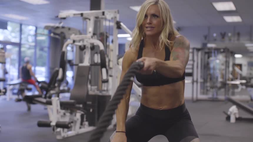 White woman exercises with a pair of heavy ropes in a fitness gym