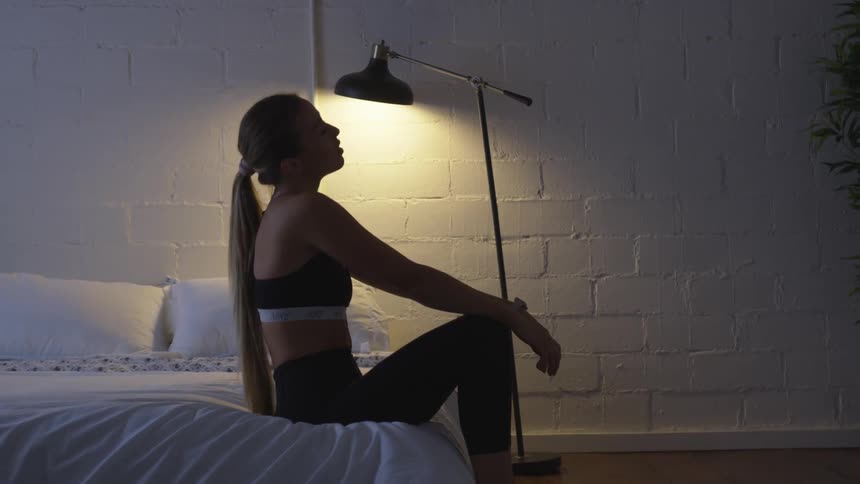 Young woman in a fitness apparel sits on a bed