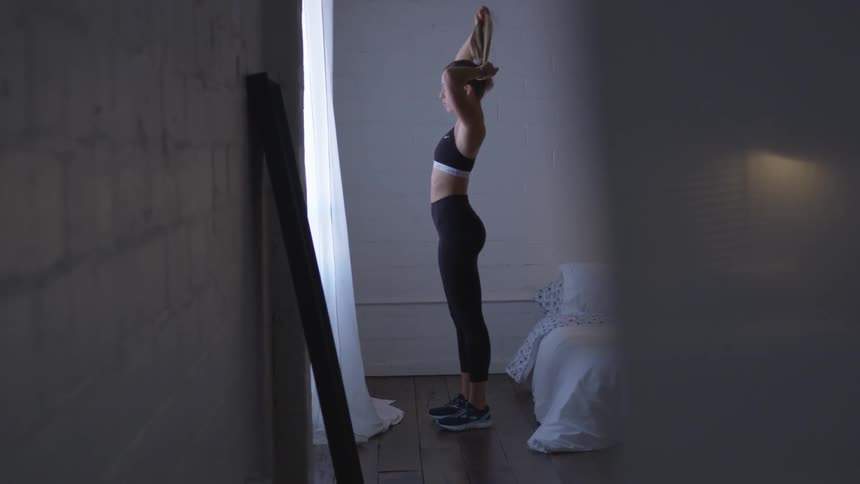A white woman ties her hair into a ponytail and then leaves the room