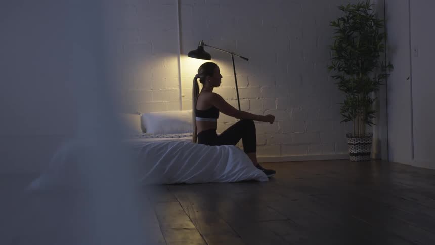 A woman stretching while sitting on a bed