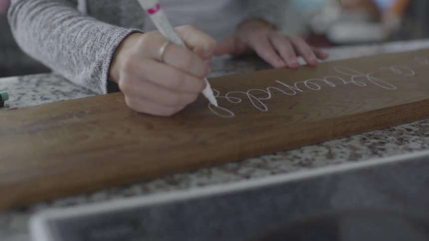 Woman writes calligraphy script with paint pen on wooden board