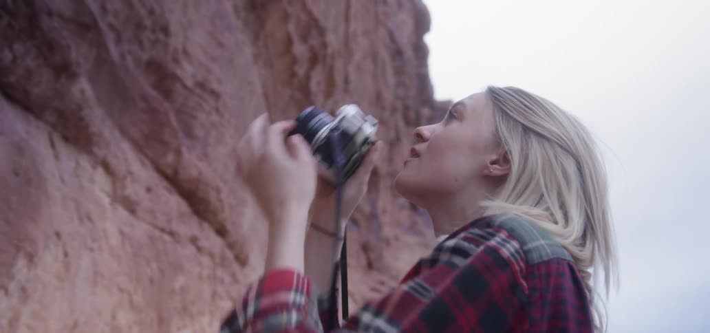 A blonde woman takes a picture of a rock formation