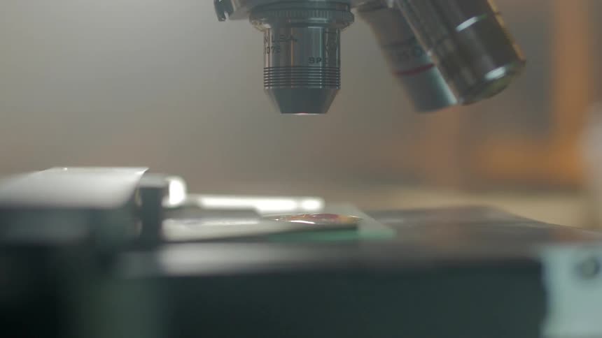 Close view of a technician manipulating a slide on a microscope