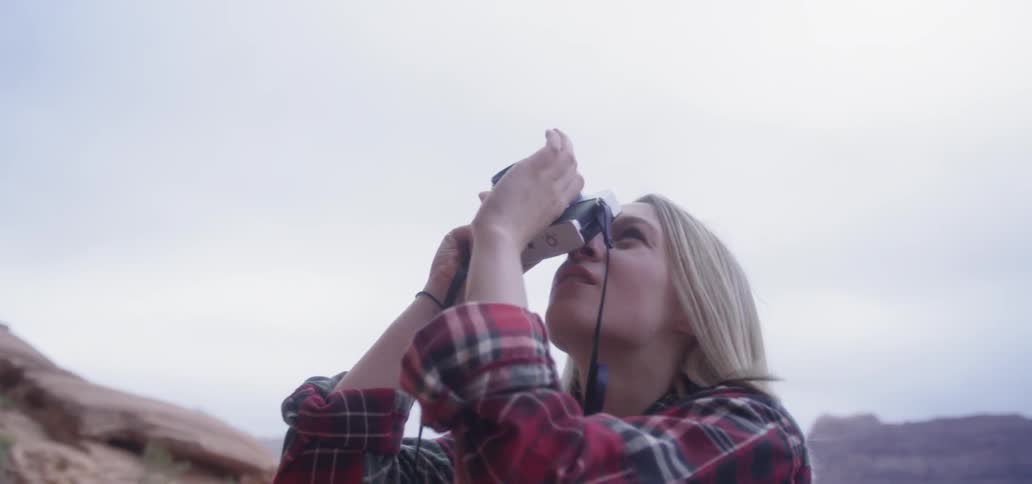 A blonde female caucasian taking photos with a camera outside