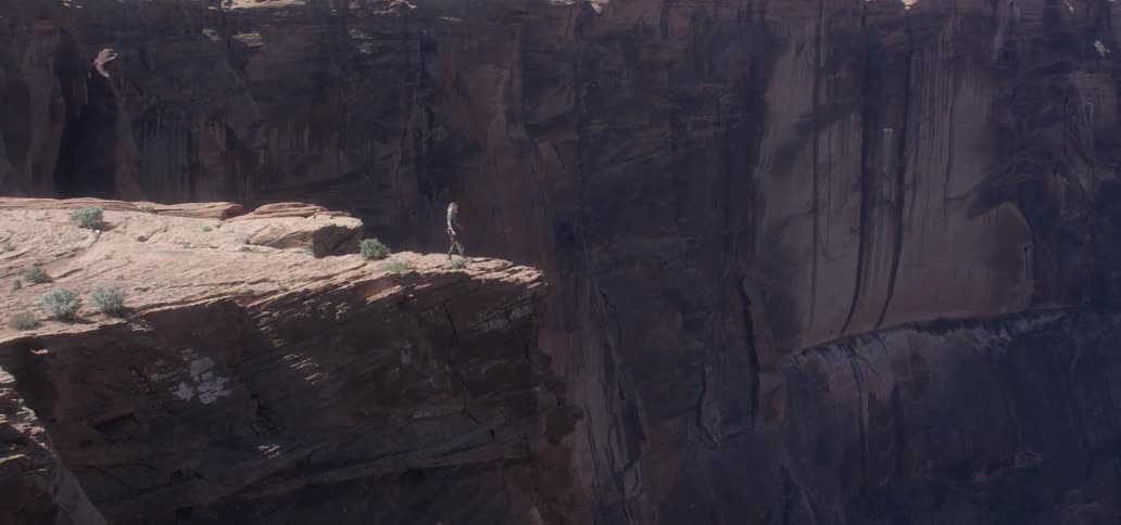 A hiker walks up to the edge of a cliff and takes a photograph in the wilderness