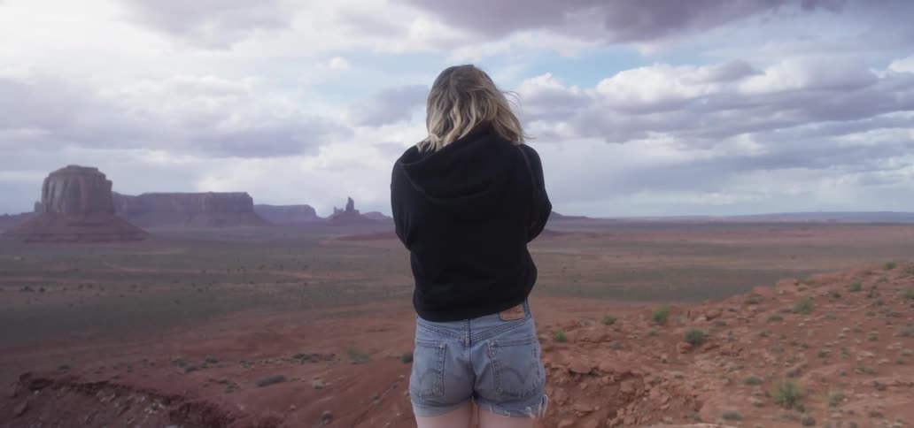 A woman stands near a cliff edge and takes a picture with a camera