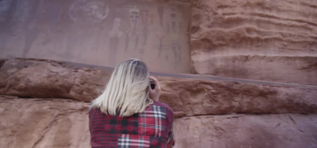 A blonde female standing near a large stone monument