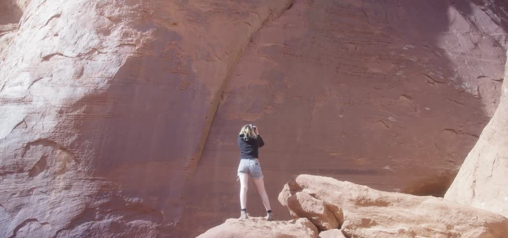 A woman takes a photo while standing on the edge of a cliff