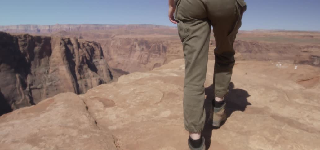 A woman hikes to the top of a red mountain to get a view of a lake in the valley below